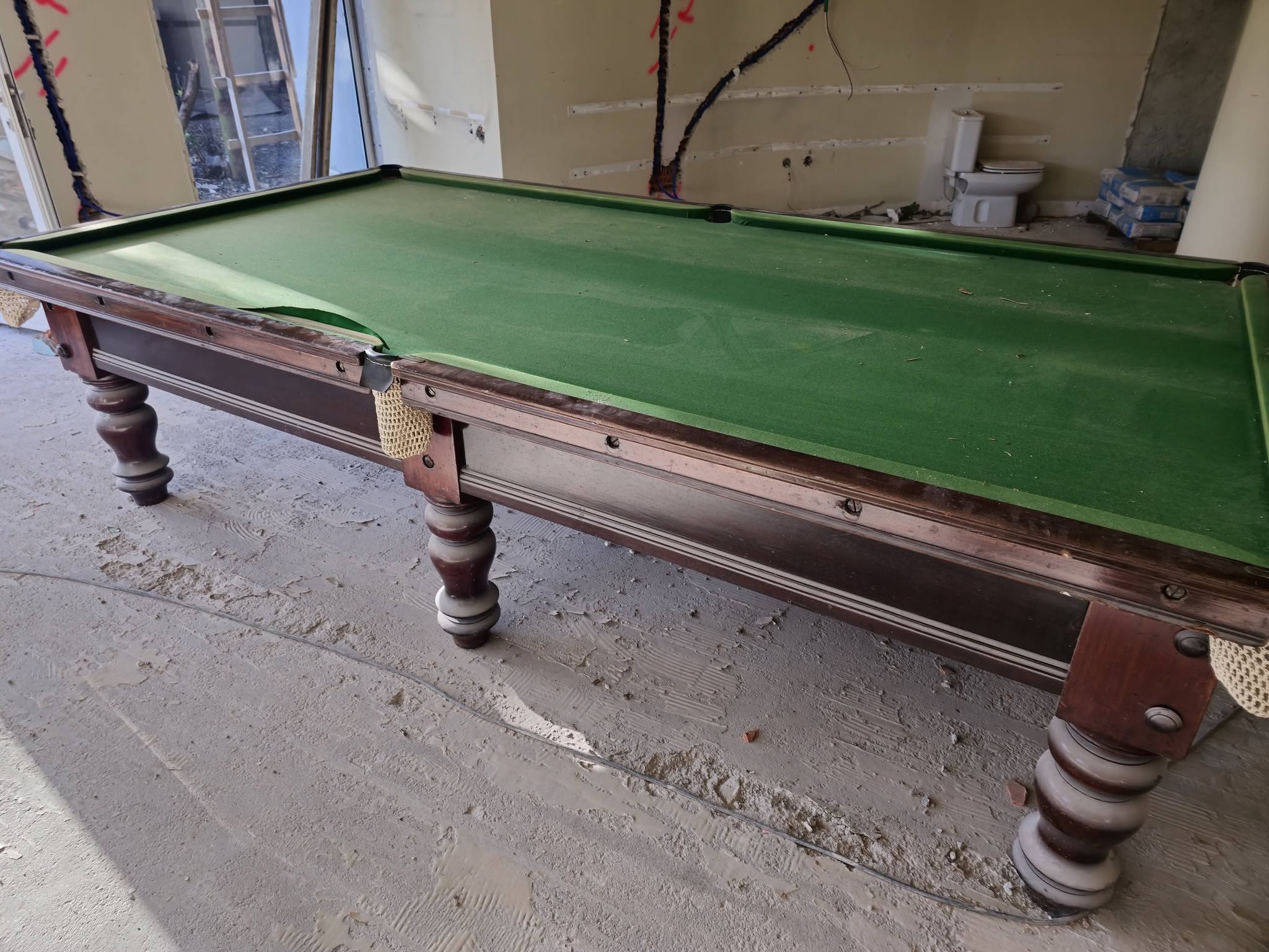 Mesa de snooker antiga abandonada em obra, com pano rasgado e madeira degradada